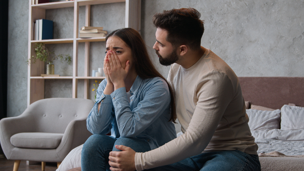 Mężczyzna pocieszający płaczącą kobietę, siedzącą na łóżku w sypialni