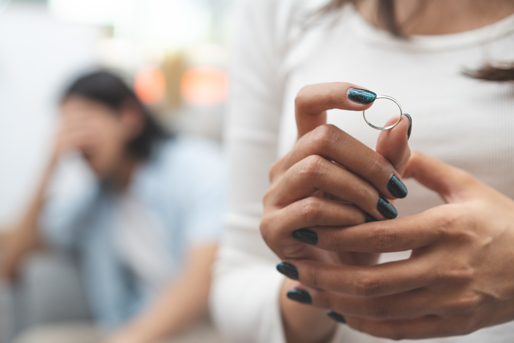 Kobieta siedząca obok swojego partnera i trzymająca zdjętą z palca obrączkę w dłoni
