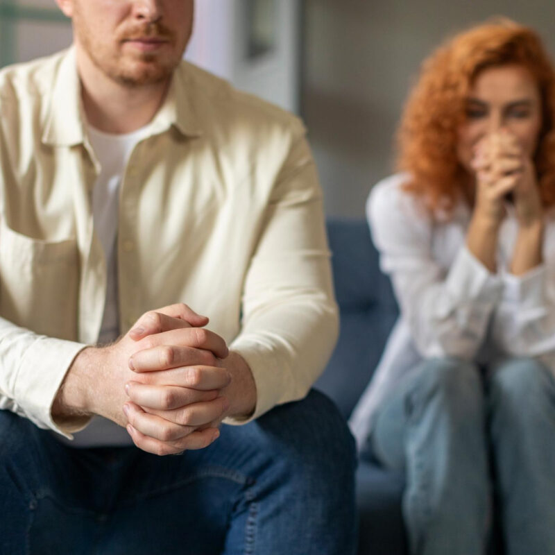 Mężczyzna z zaplecionymi dłońmi i zaniepokojona kobieta siedzą wspólnie na kanapie