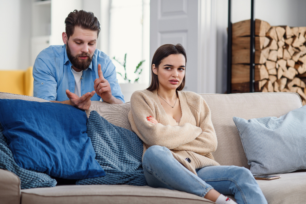 Mężczyzna wyliczający błędy siedzącej na sofie kobiecie, która go zdradziła