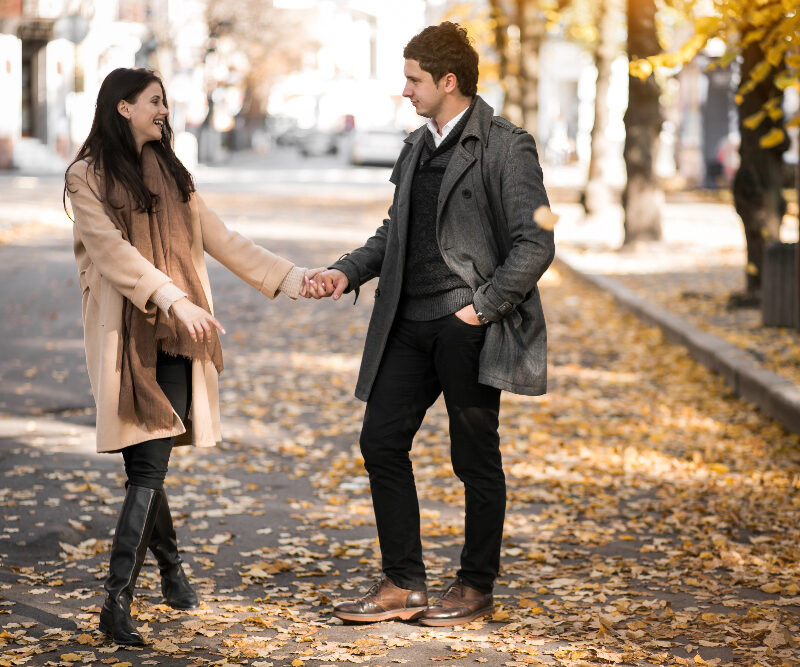 Szczęśliwa para w młodym wieku chodząca po alejce obsypanej liśćmi w trakcie jesieni